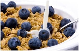 A bowl of cereal with blueberries and a spoon.