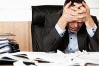 A stressed man sitting at a desk cluttered with papers.