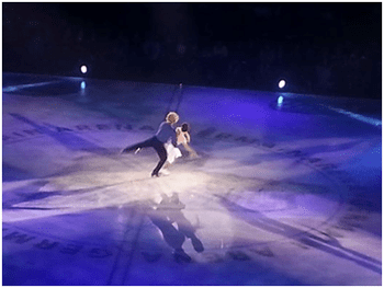 Figure skaters performing a lift on ice under blue lights.