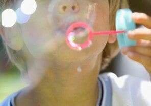 A child blowing bubbles outdoors on a sunny day.
