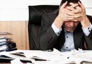 A stressed man sitting at a desk cluttered with papers.