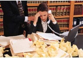 A stressed woman lawyer on the phone amid piles of paperwork.